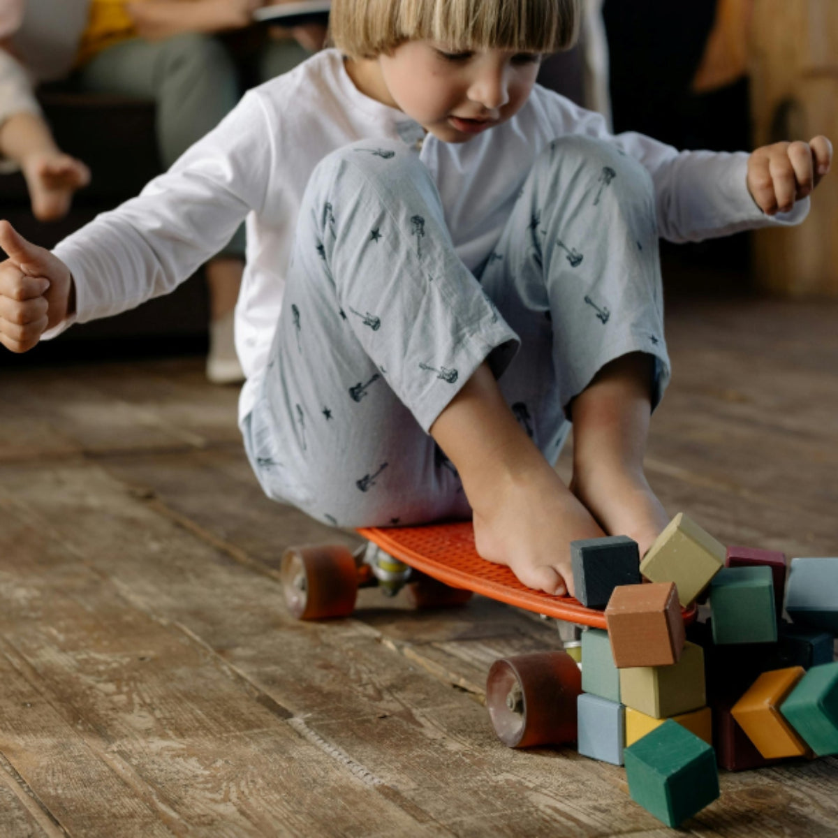 Child playing with a skateboard and blocks on a wooden floor